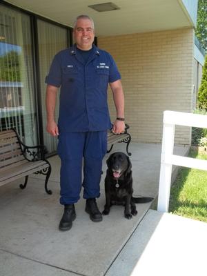 Coast Guard worker standing and black lab on leash sitting next to person